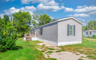 Gray manufactured home with a wooden entry deck at 1023 E. 9th Street, Lot 6, Mountain Home, Arkansas.