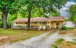 Front exterior of 809 Langston Street in Mountain Home, Arkansas, with a covered porch, attached carport and mature shade trees.